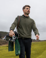 Merino Haven Hoodie in green, carrying a golf bag on the course