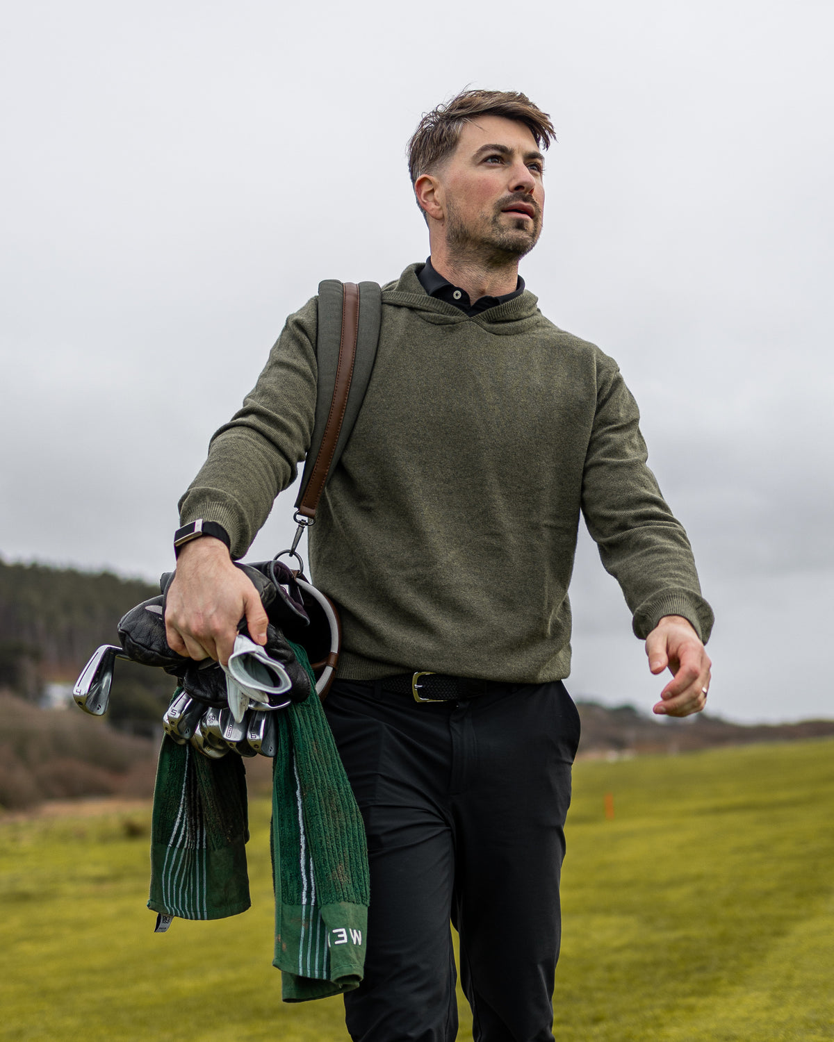 Merino Haven Hoodie in green, carrying a golf bag on the course