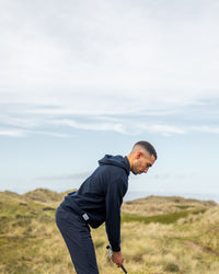 Merino Haven Hoodie in navy, addressing the ball in the dunes